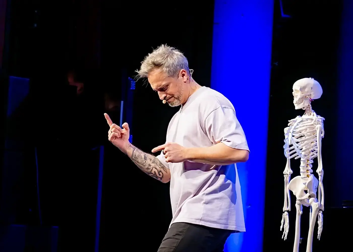 der-physiopath-bühne-entertainer-physiotherapie-skelett Der Physiopath auf der Bühne mit Mikrofon und Skelettmodell während seiner Show.