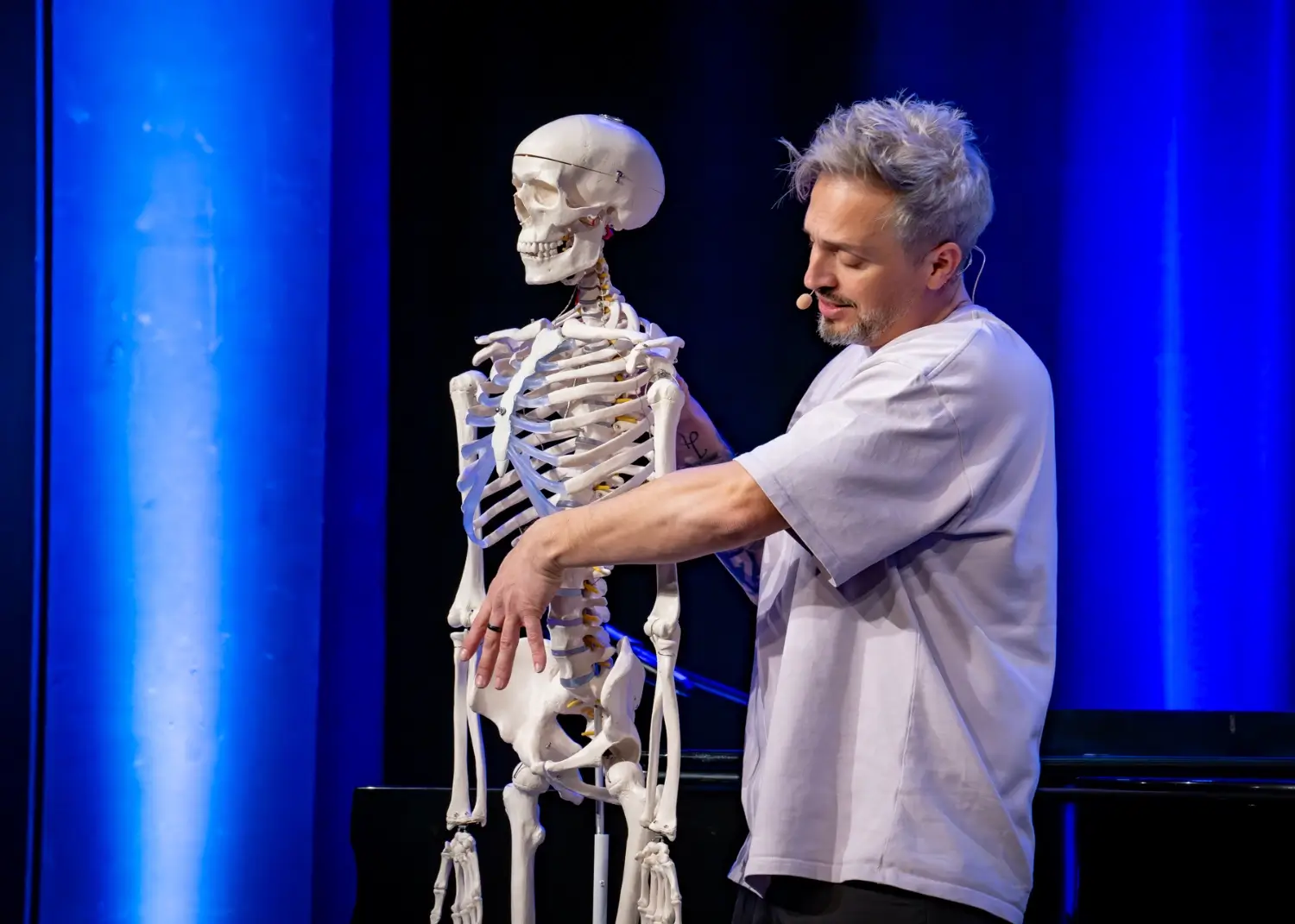 der-physiopath-bühne-skelett-physiotherapie-entertainer Der Physiopath demonstriert an einem Skelettmodell während seiner Show auf der Bühne.